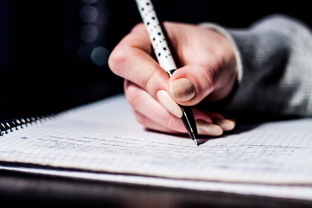 A manicured hand holds a pen and writes in a notebook.