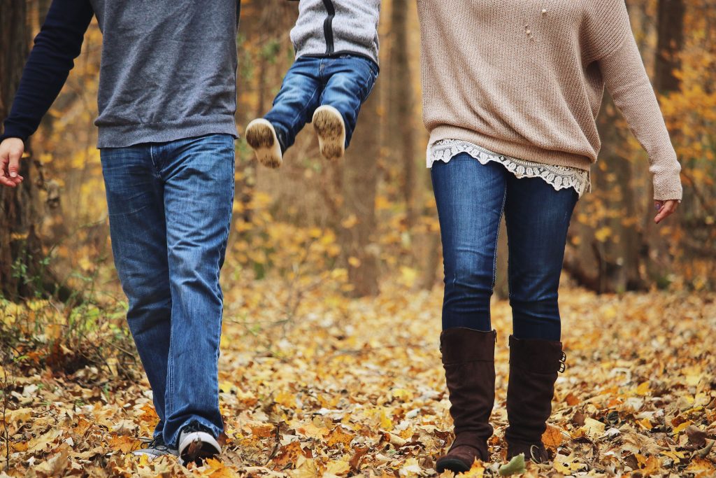 Two adults happily lifting a child in the air while walking in the woods